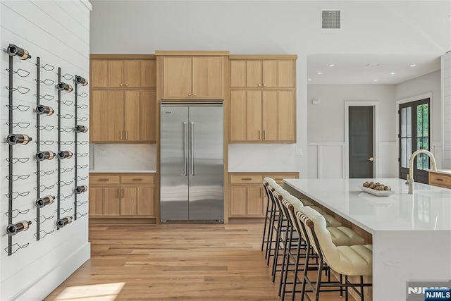 kitchen featuring visible vents, a breakfast bar, light countertops, light wood-style floors, and stainless steel built in refrigerator