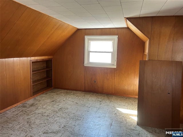 additional living space with light floors, wooden walls, and vaulted ceiling