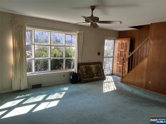 unfurnished living room with stairway, plenty of natural light, wooden walls, and visible vents