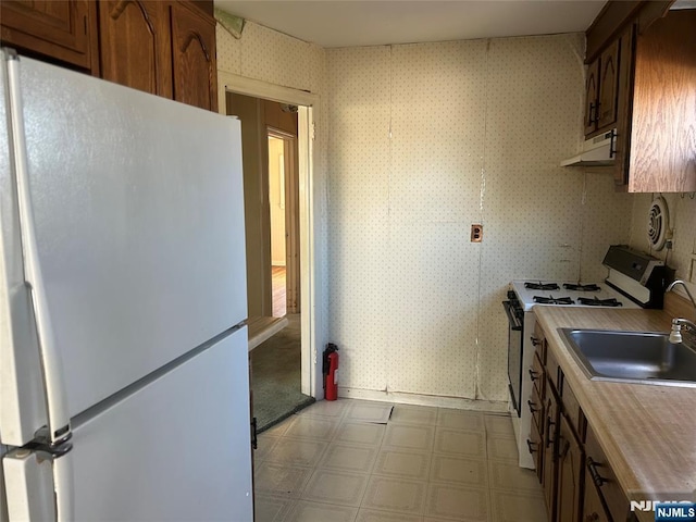 kitchen with light floors, a sink, white appliances, under cabinet range hood, and wallpapered walls