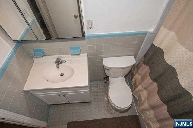 bathroom featuring a wainscoted wall, vanity, toilet, and tile walls