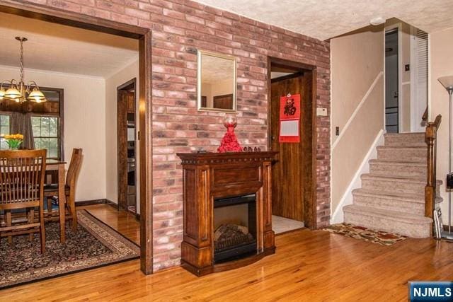 interior space with brick wall, stairway, wood finished floors, a fireplace, and a chandelier