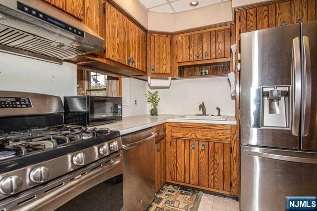 kitchen featuring a sink, light countertops, appliances with stainless steel finishes, range hood, and brown cabinetry