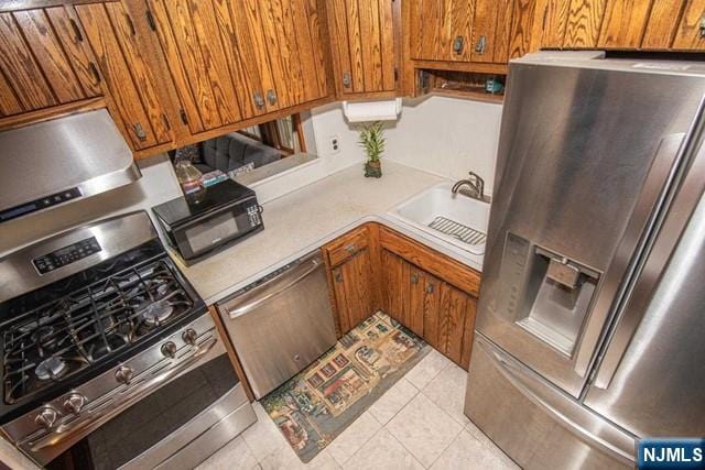 kitchen featuring stainless steel appliances, light countertops, brown cabinetry, light tile patterned flooring, and a sink