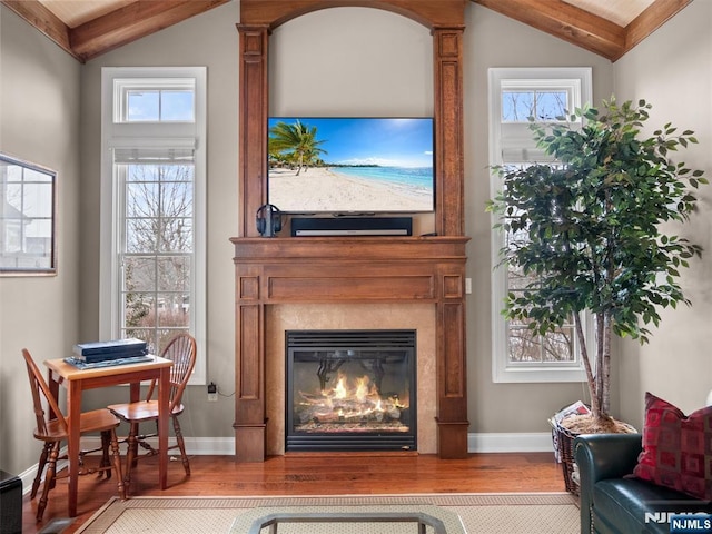 interior space featuring a glass covered fireplace, vaulted ceiling with beams, baseboards, and wood finished floors