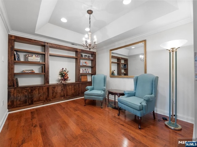 sitting room with a tray ceiling, a notable chandelier, ornamental molding, baseboards, and hardwood / wood-style flooring