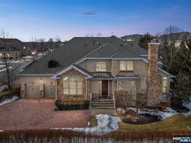 view of front of house with decorative driveway, a chimney, stucco siding, a garage, and stone siding