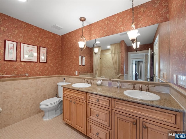 bathroom featuring a wainscoted wall, visible vents, a sink, and wallpapered walls