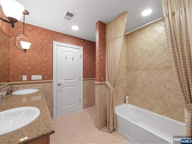 bathroom with visible vents, a sink, tile walls, and wallpapered walls