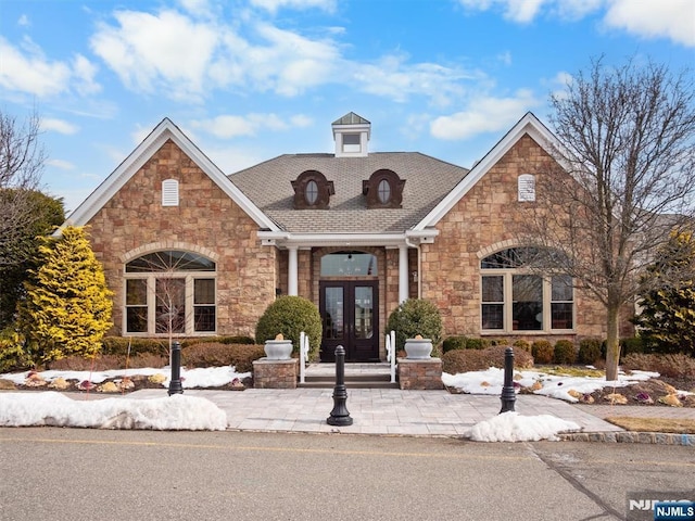 view of front facade with stone siding, roof with shingles, and french doors