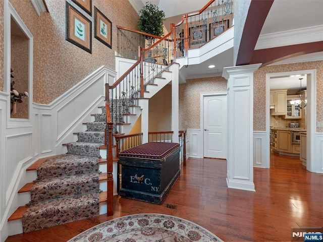 staircase with ornate columns, ornamental molding, wainscoting, and wallpapered walls