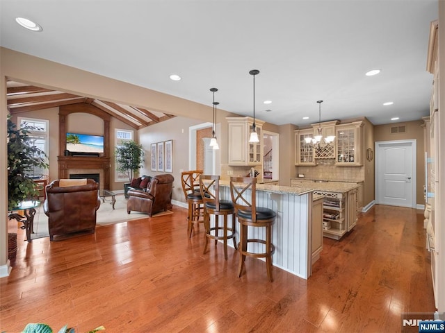 kitchen featuring cream cabinetry, a breakfast bar area, hanging light fixtures, glass insert cabinets, and open floor plan