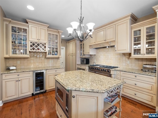 kitchen with wine cooler, a kitchen island, appliances with stainless steel finishes, glass insert cabinets, and pendant lighting