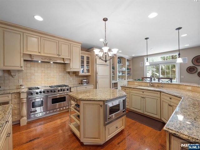 kitchen with a sink, appliances with stainless steel finishes, a center island, decorative light fixtures, and custom range hood