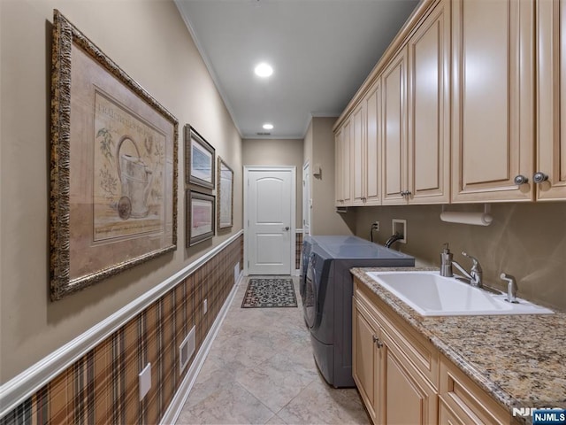 clothes washing area featuring washing machine and dryer, a wainscoted wall, a sink, cabinet space, and crown molding