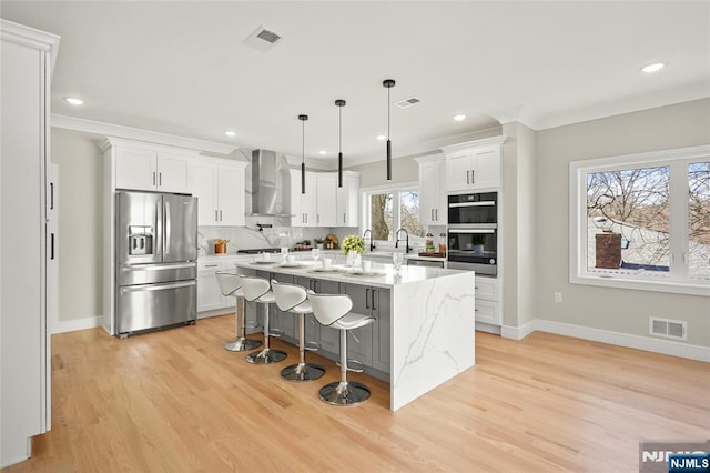 kitchen with double oven, visible vents, wall chimney range hood, decorative backsplash, and stainless steel fridge