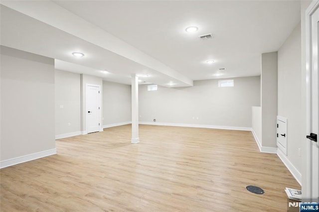 finished below grade area with light wood-style floors, visible vents, and baseboards