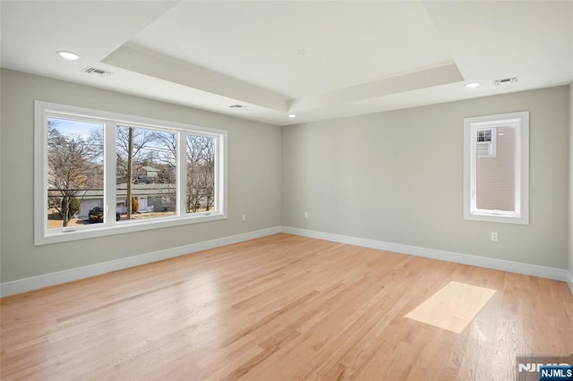 empty room with light wood finished floors, baseboards, visible vents, and a raised ceiling