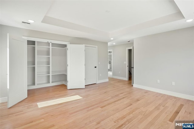 unfurnished bedroom featuring baseboards, a tray ceiling, light wood-style flooring, and recessed lighting