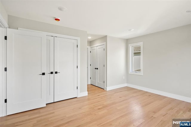 unfurnished bedroom featuring light wood finished floors, baseboards, and multiple closets