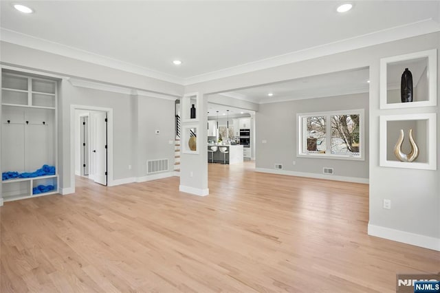 unfurnished living room featuring stairway, visible vents, light wood-style floors, and ornamental molding