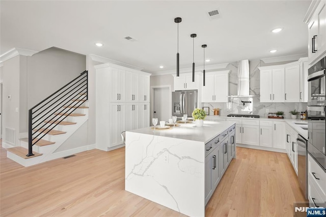 kitchen featuring wall chimney exhaust hood, light wood finished floors, white cabinetry, and stainless steel appliances