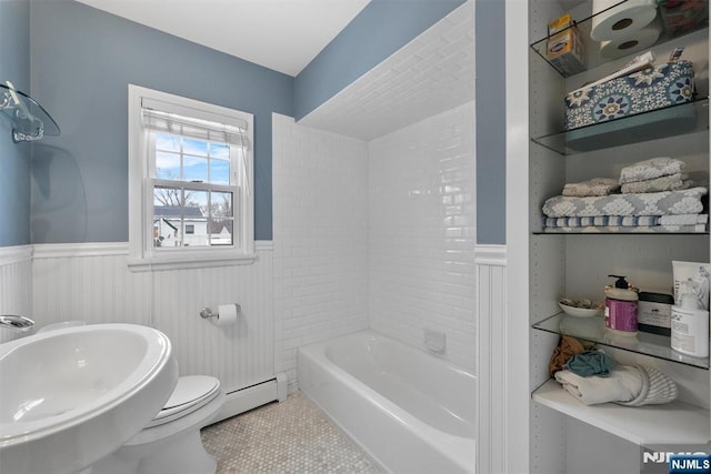 bathroom with tile patterned flooring, toilet, a sink, baseboard heating, and wainscoting