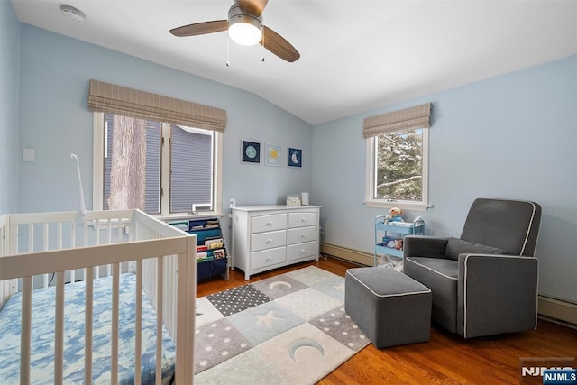 bedroom with lofted ceiling, a ceiling fan, a baseboard heating unit, wood finished floors, and a nursery area