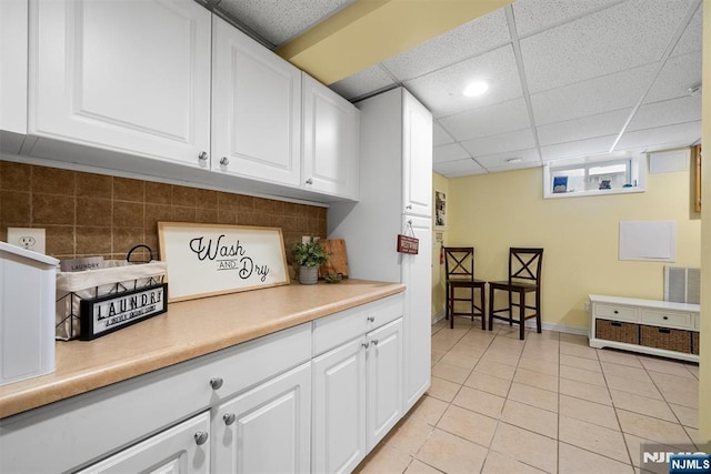 kitchen with light tile patterned floors, a paneled ceiling, light countertops, and white cabinetry