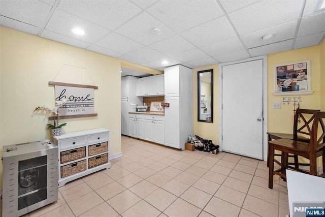 kitchen featuring light tile patterned flooring, a paneled ceiling, a fireplace, white cabinetry, and light countertops