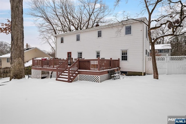 snow covered back of property with fence and a deck