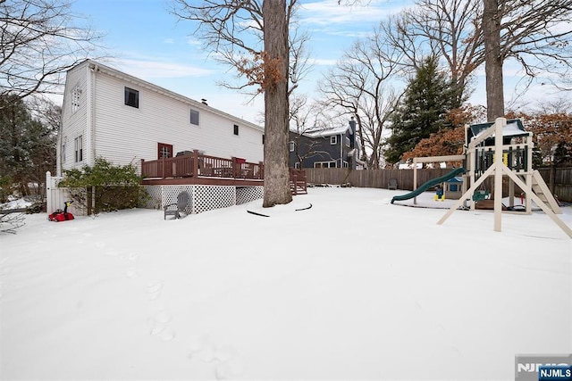 yard covered in snow with a playground, fence, and a deck