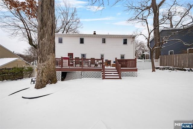 snow covered back of property featuring fence and a deck