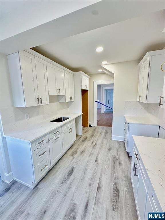 kitchen featuring light wood-type flooring, light stone countertops, baseboards, and white cabinetry