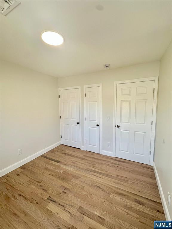 unfurnished bedroom with light wood-style flooring, multiple closets, visible vents, and baseboards