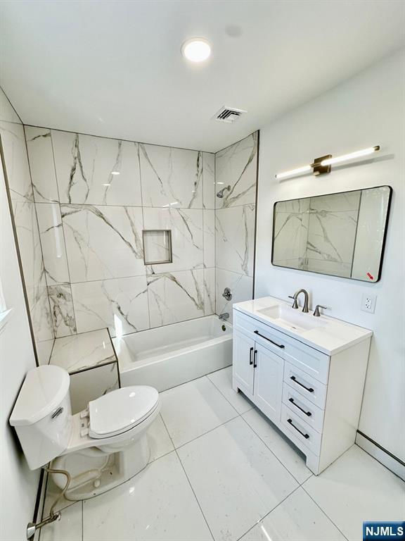 bathroom with toilet, visible vents, vanity, marble finish floor, and washtub / shower combination