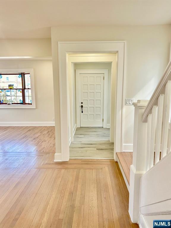 corridor with light wood-type flooring, baseboards, and stairs