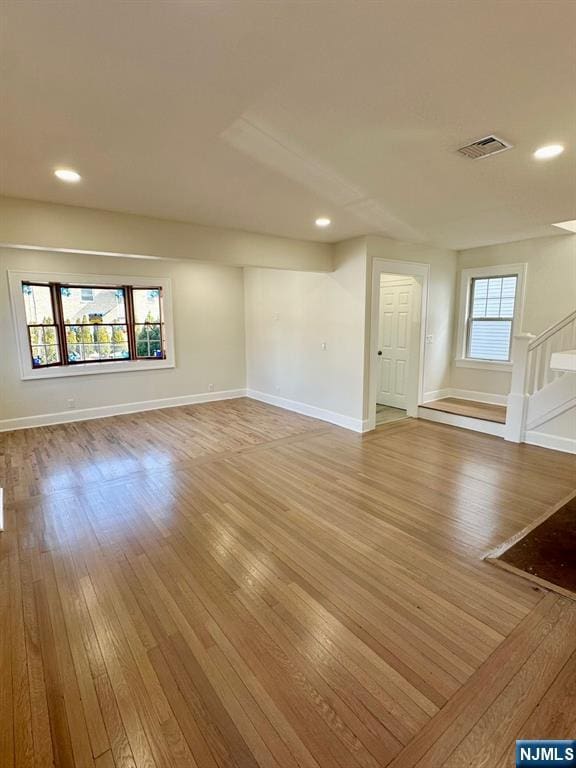 unfurnished living room featuring light wood finished floors, stairs, visible vents, and a wealth of natural light