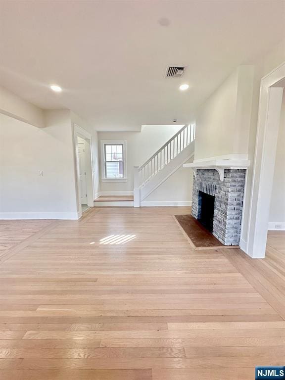 unfurnished living room with stairs, a fireplace, visible vents, and light wood-style floors