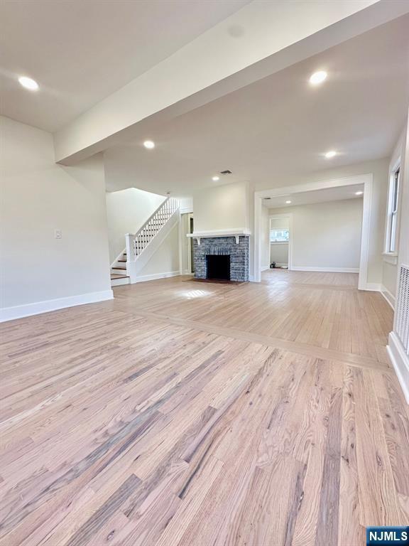 unfurnished living room featuring baseboards, light wood-style flooring, stairway, a fireplace, and recessed lighting