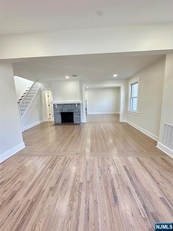 unfurnished living room with visible vents, light wood-style flooring, a fireplace with flush hearth, baseboards, and stairs