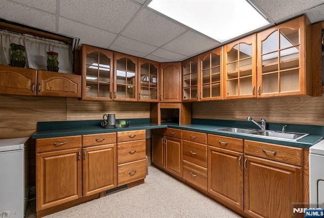 kitchen featuring light carpet, a drop ceiling, a sink, and brown cabinets