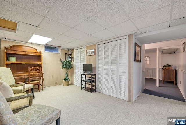 living area featuring wood walls, carpet, and a paneled ceiling