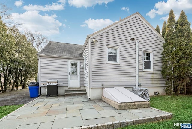 rear view of property with entry steps, a patio, a shingled roof, and a lawn