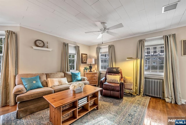 living area featuring radiator heating unit, wood-type flooring, visible vents, and crown molding