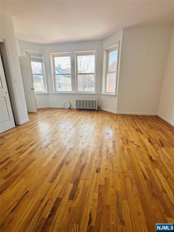 unfurnished bedroom featuring light wood-type flooring, baseboards, multiple windows, and radiator heating unit