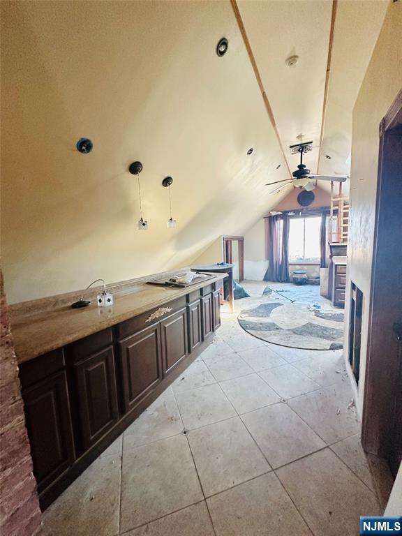 interior space featuring light tile patterned flooring, vaulted ceiling, light countertops, dark brown cabinets, and pendant lighting