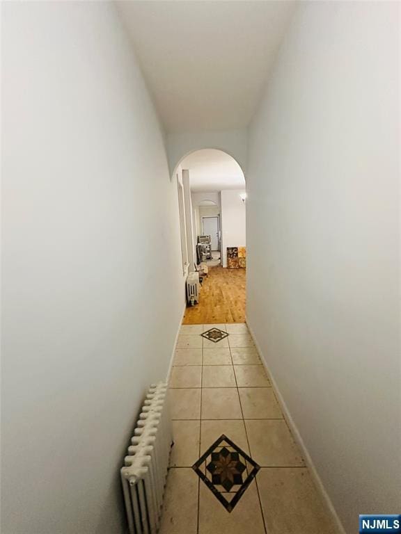 corridor with arched walkways, radiator, baseboards, and light tile patterned floors