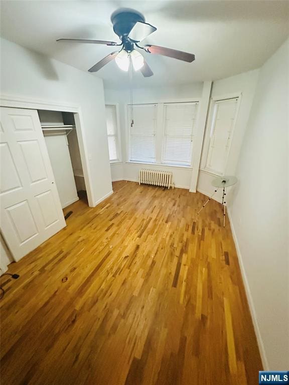 unfurnished bedroom featuring a closet, radiator heating unit, light wood-style floors, a ceiling fan, and baseboards