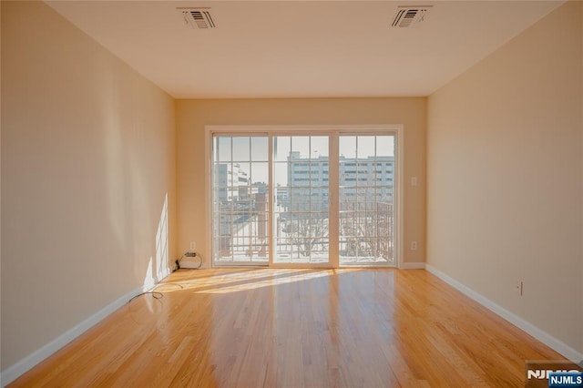 empty room with a view of city, light wood-style flooring, visible vents, and baseboards